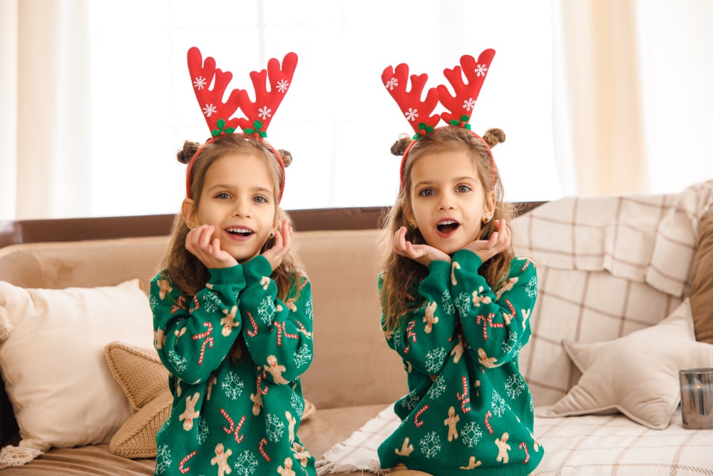 Cute sisters in matching green Christmas sweatshirts with deer designs Two little girls in green Christmas sweaters with deer motifs